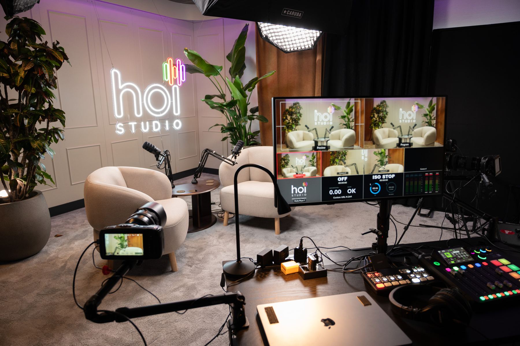 Hoi Studio podcast studio, with neon logo sign, lounge seating, multi-camera switcher and live program monitor